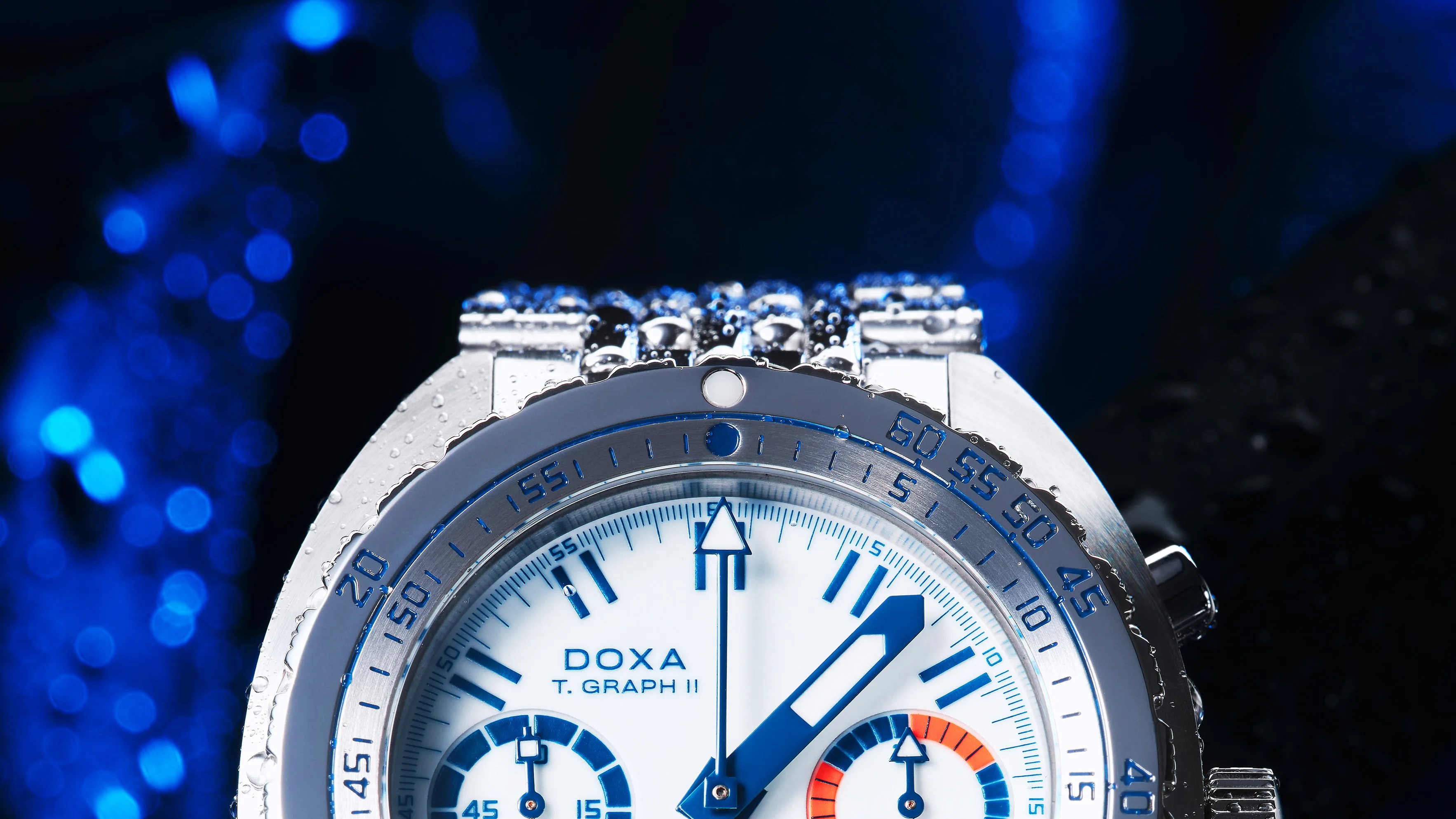 Close-up of a silver DOXA T. GRAPH II watch with blue and orange details and water droplets on the bezel.