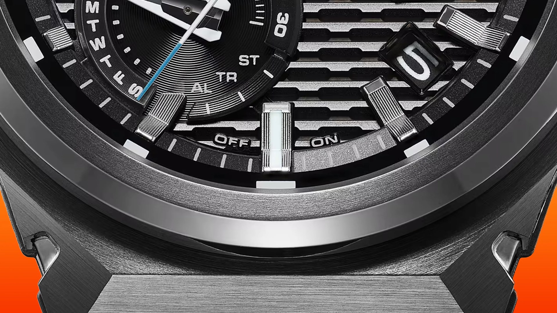 Close-up of a black and silver watch face showing day indicators, a date window displaying "5," and an "OFF" and "ON" switch indicator.