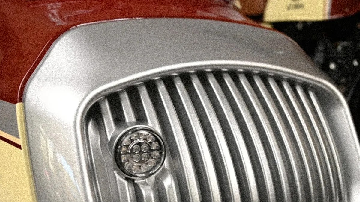 Close-up of a silver motorcycle front grille with a round LED light on a red and cream body.