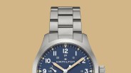 Close-up of a silver metal watch band and part of a blue Hamilton watch face with white and beige hands.