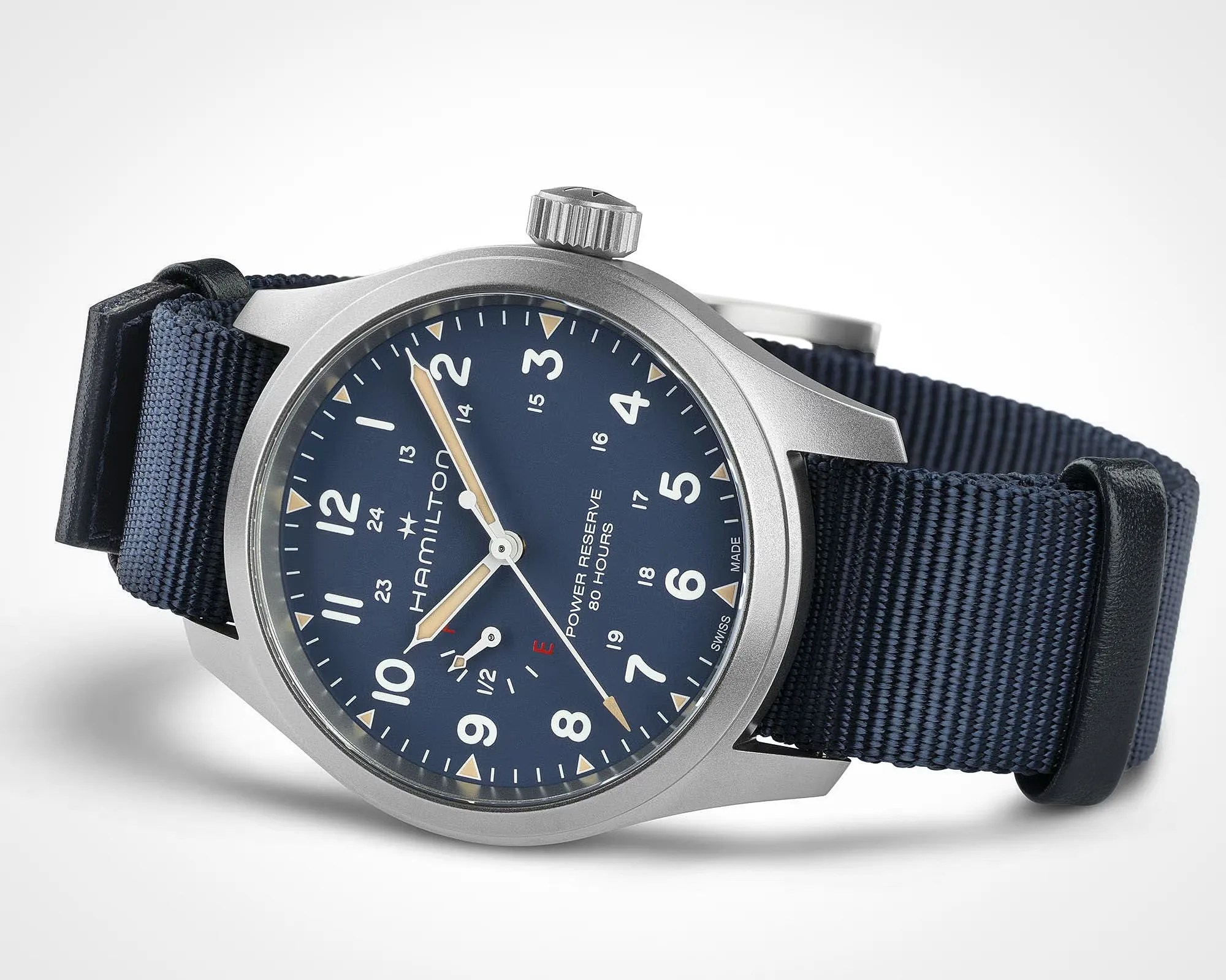 Close-up of a Hamilton wristwatch with a blue dial, beige hands, silver case, and navy blue fabric strap.