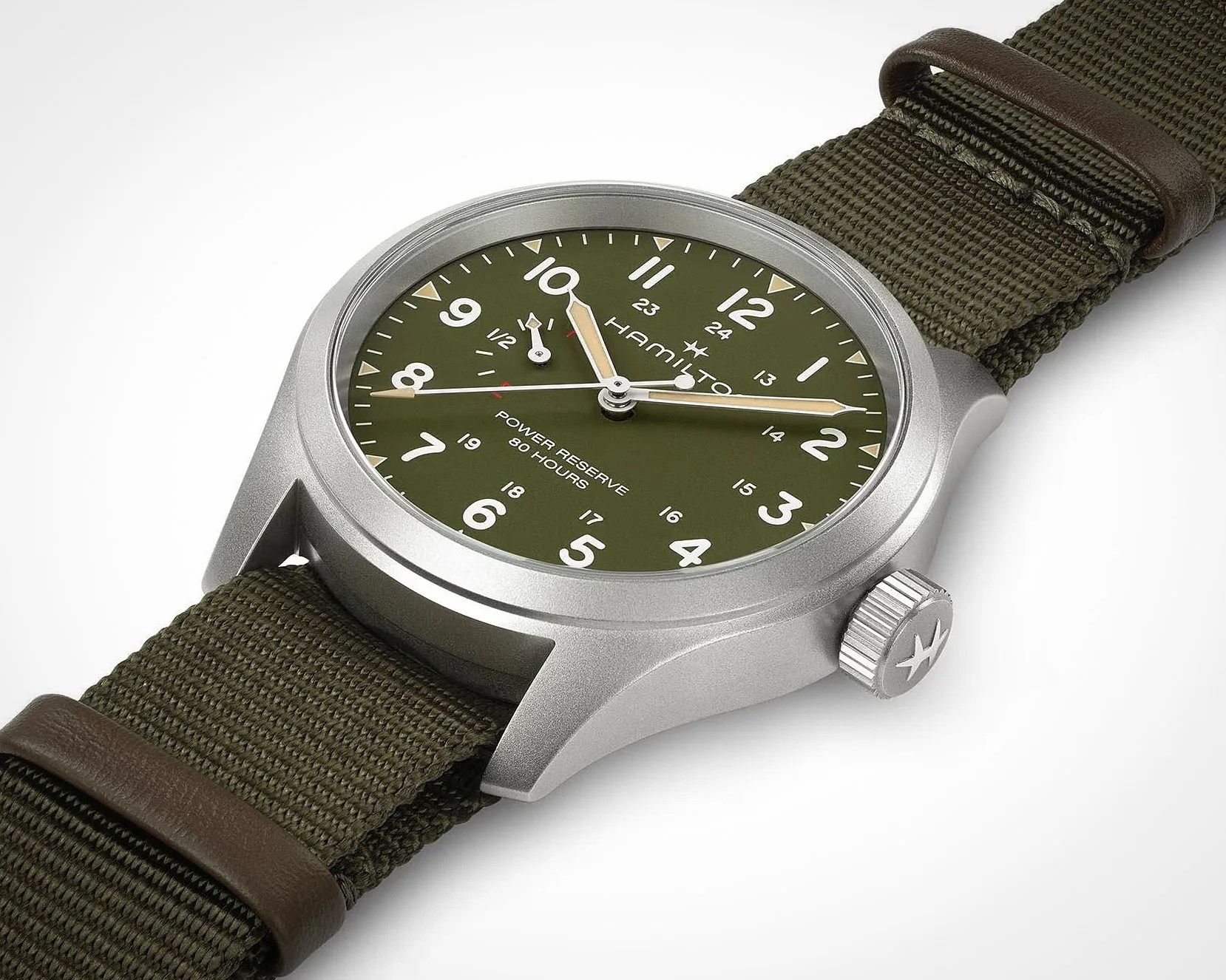 Hamilton watch with olive green dial, white numerals, beige hands, silver case, and green fabric strap with brown leather loops.