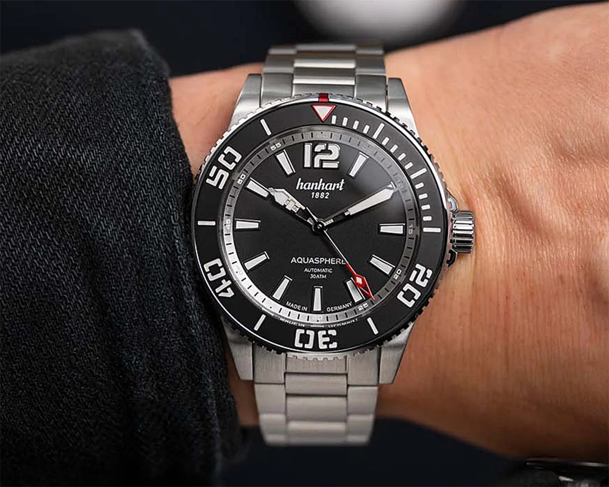 Silver metal wristwatch with black dial and bezel, white hour markers, and red-tipped second hand worn on a wrist.