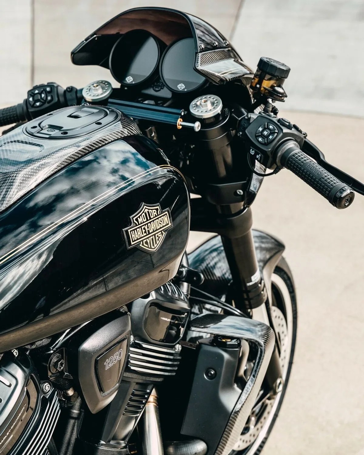 Close-up of a black Harley-Davidson motorcycle fuel tank and handlebars with carbon fiber accents.