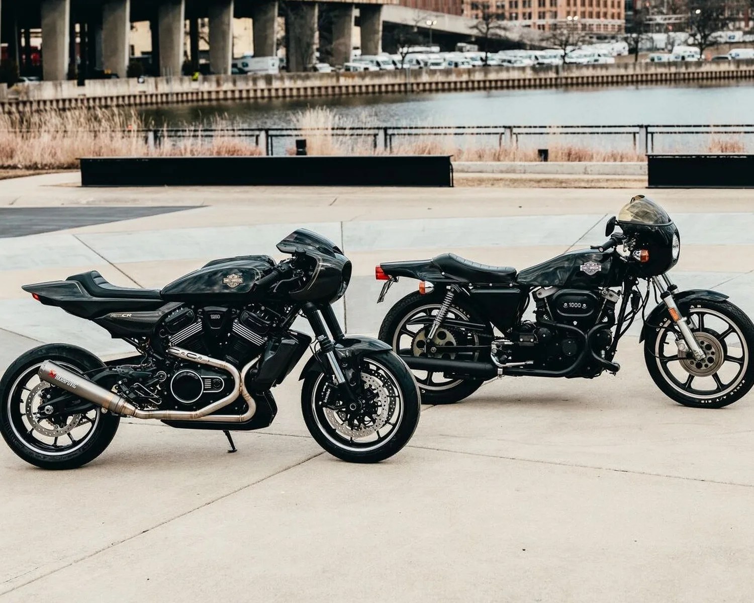 Two black Harley-Davidson motorcycles parked on a concrete surface near a body of water.