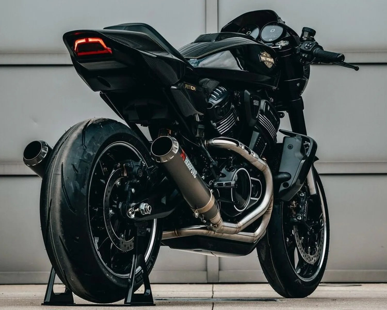 Black Harley-Davidson motorcycle with dual Akrapovic exhaust pipes and wide rear tire on stands.