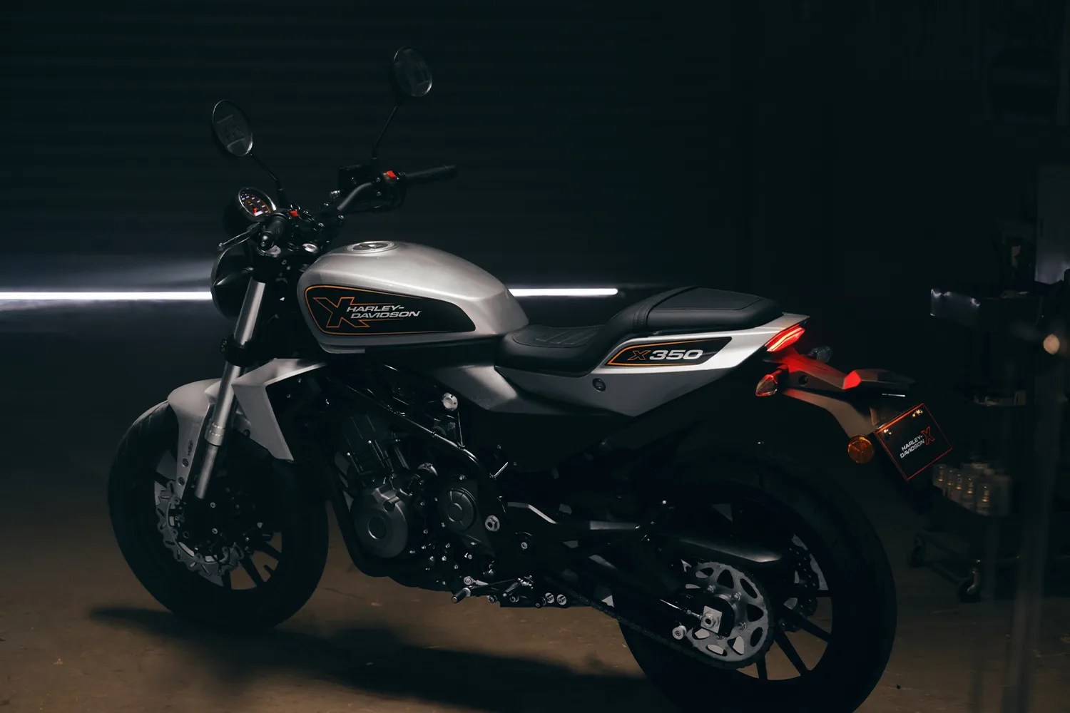 Silver Harley-Davidson X350 motorcycle with black seat and orange accents in a dimly lit garage.