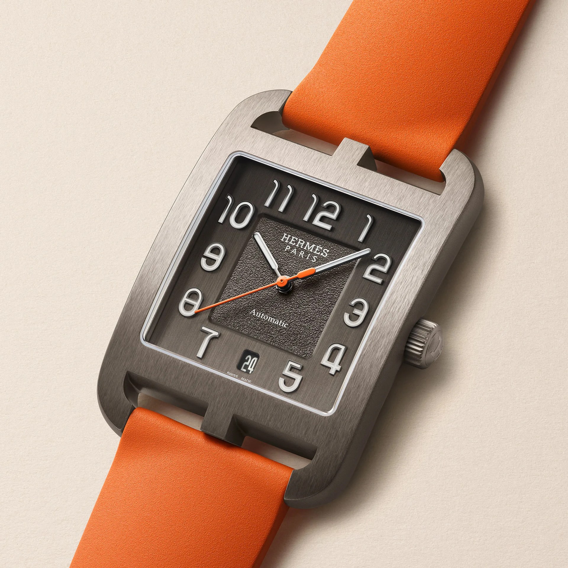 Herm&egrave;s Paris wristwatch with a rectangular brushed metal case, black textured dial, white numerals, and an orange rubber strap.