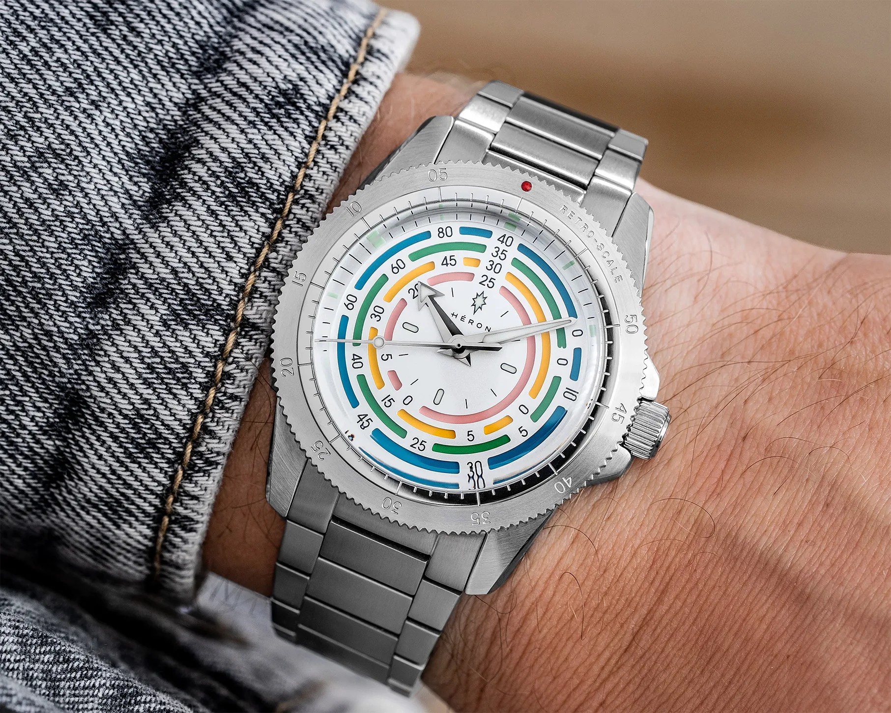 Stainless steel wristwatch with colorful concentric arcs on a white dial and a metal bracelet worn on a wrist.