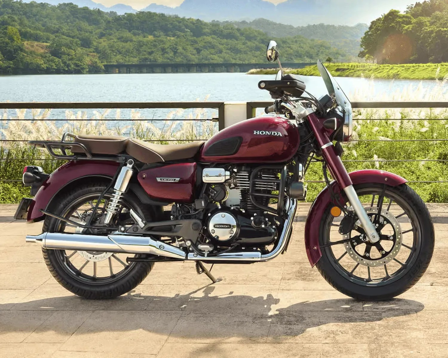 Maroon Honda motorcycle with brown seat and chrome exhaust parked on a paved area near a lake.