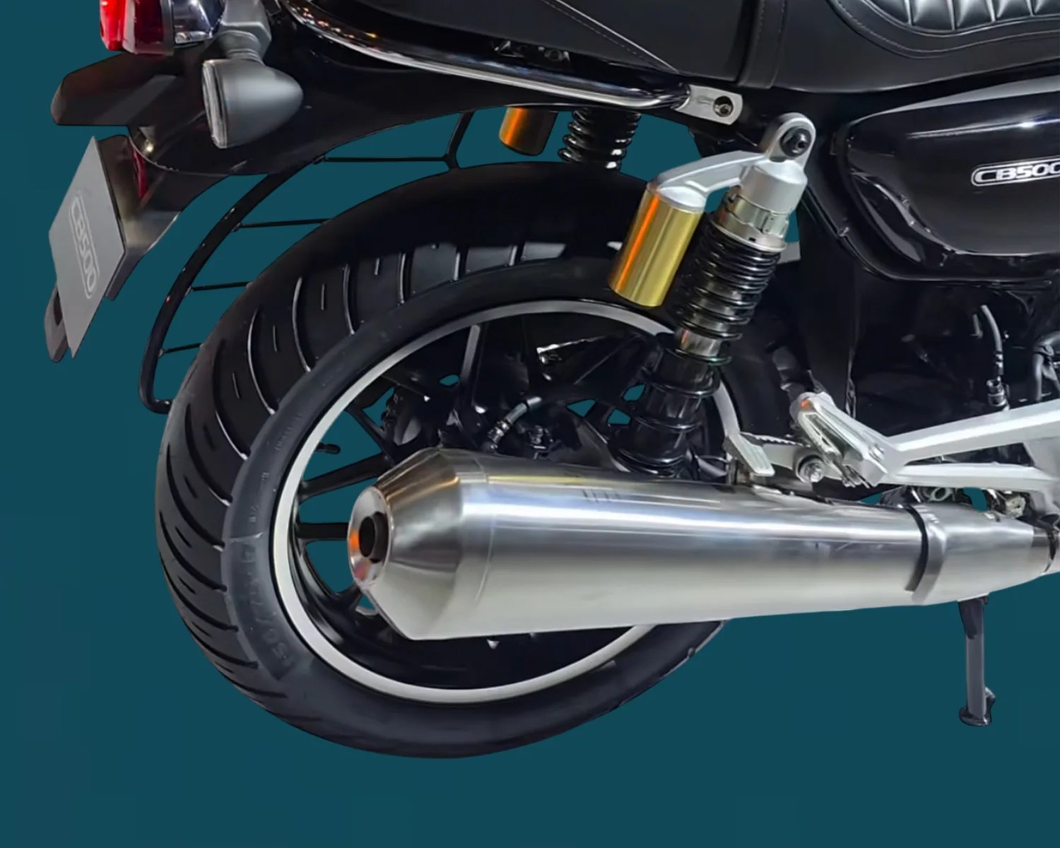 Close-up of a black motorcycle's rear wheel with a silver exhaust pipe and gold-accented suspension.