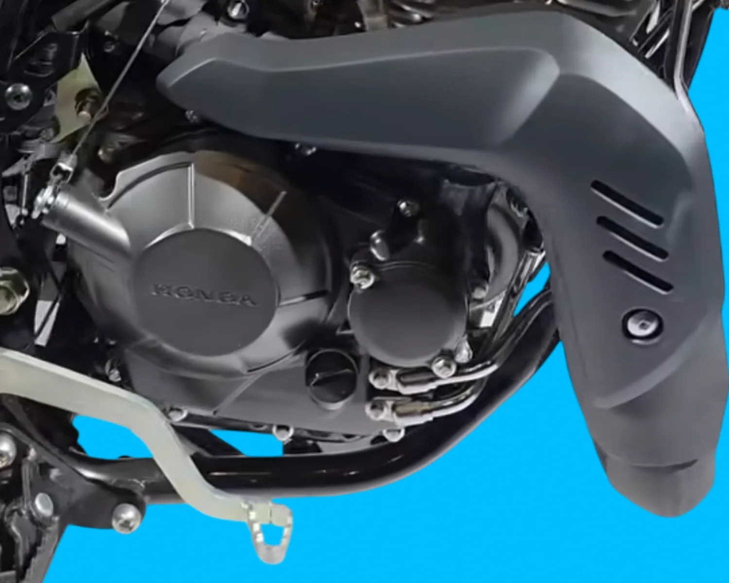 Close-up of a black Honda motorcycle engine with a silver foot pedal against a blue background.