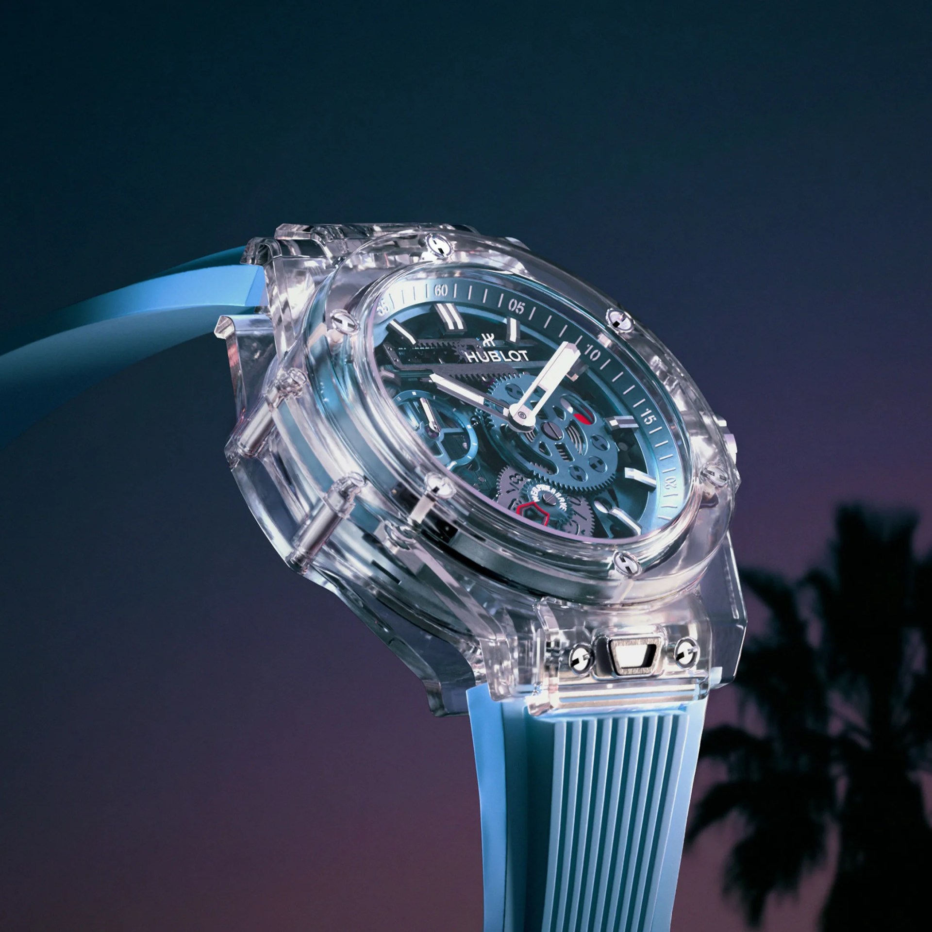 Transparent Hublot wristwatch with visible gears and a light blue ribbed strap against a dark gradient background.