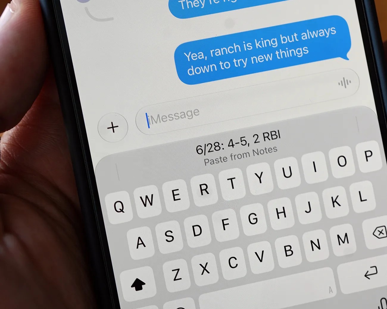 Close-up of a smartphone screen showing a text message conversation and a keyboard with a pasted note reading "6/28: 4-5, 2 RBI.