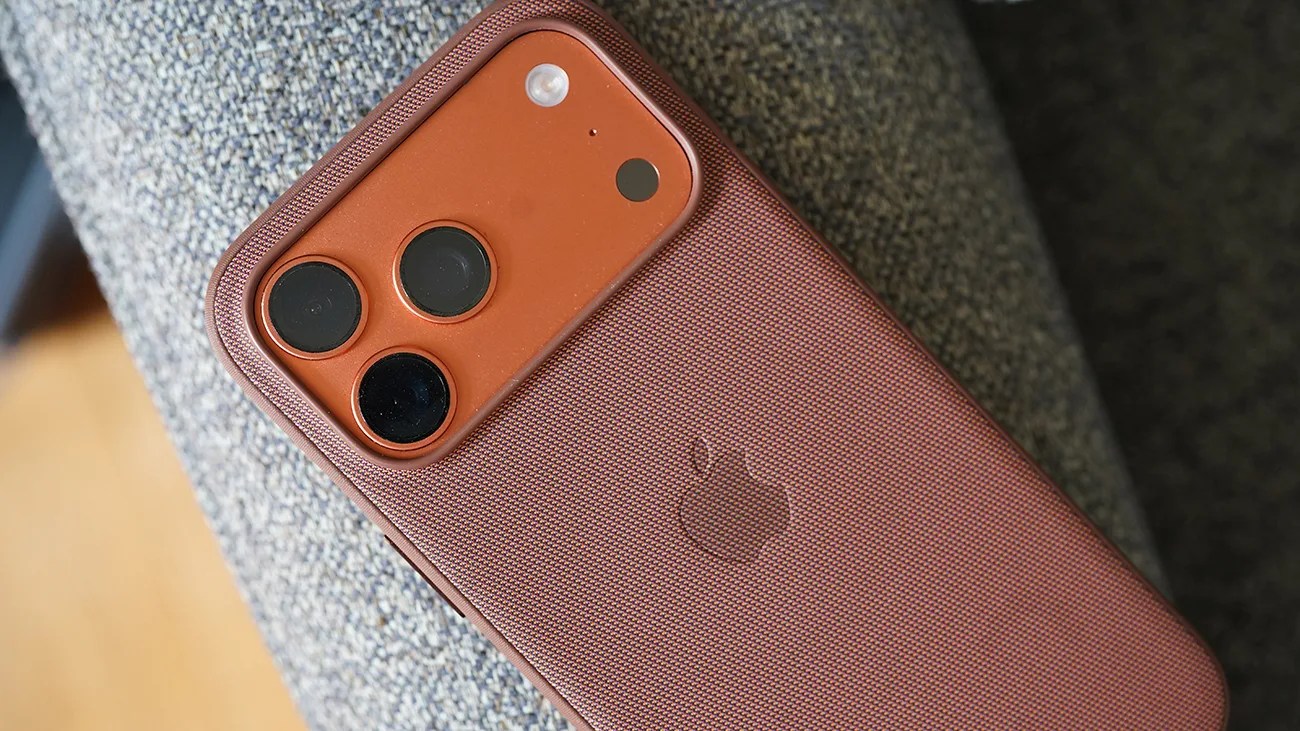 Copper-colored iPhone with triple camera lenses in a matching textured protective case on a gray fabric surface.
