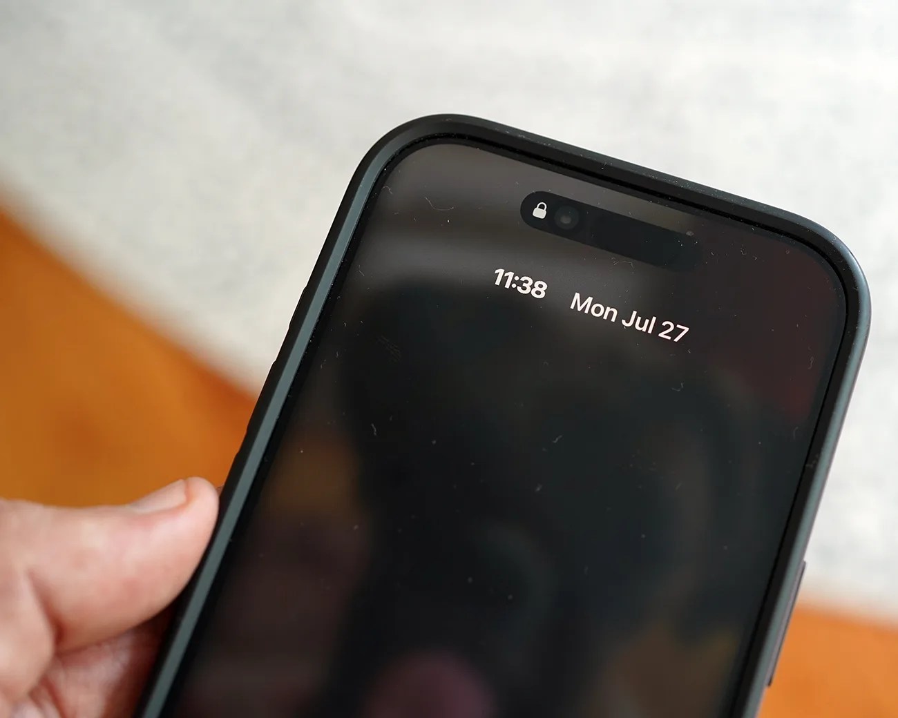 Black smartphone with a dark screen showing the time 11:38 and date Mon Jul 27, held in a hand.