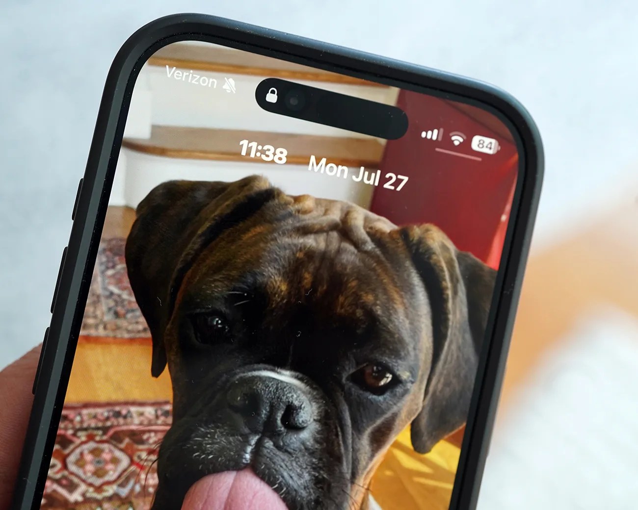 Close-up of a smartphone screen showing a brindle dog with its tongue out as the wallpaper.