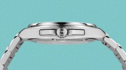 Side view of a silver stainless steel wristwatch with a crown engraved with "IWC" on a turquoise background.
