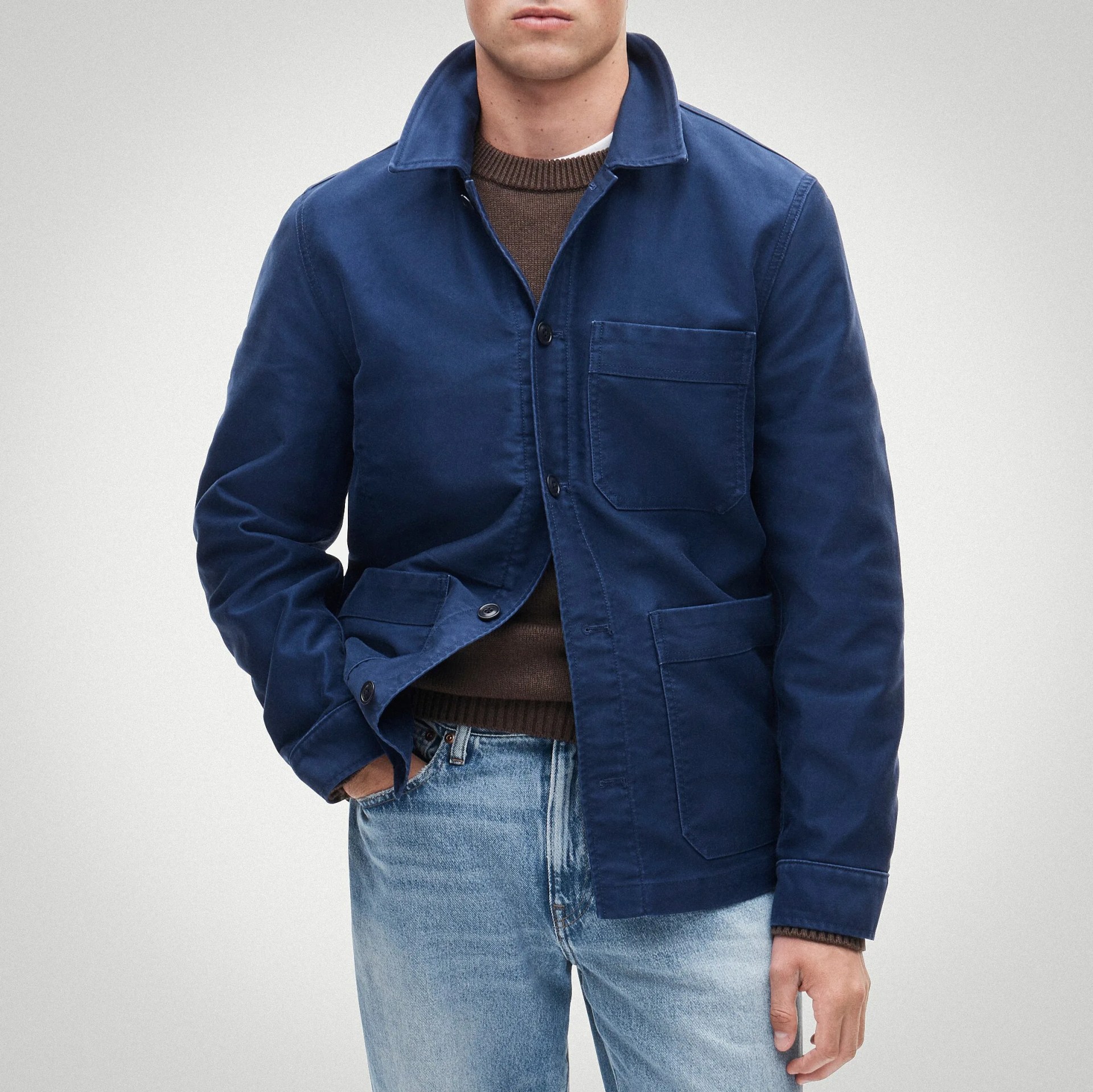 Navy blue button-up jacket with chest and lower pockets worn over a brown sweater and light blue jeans.