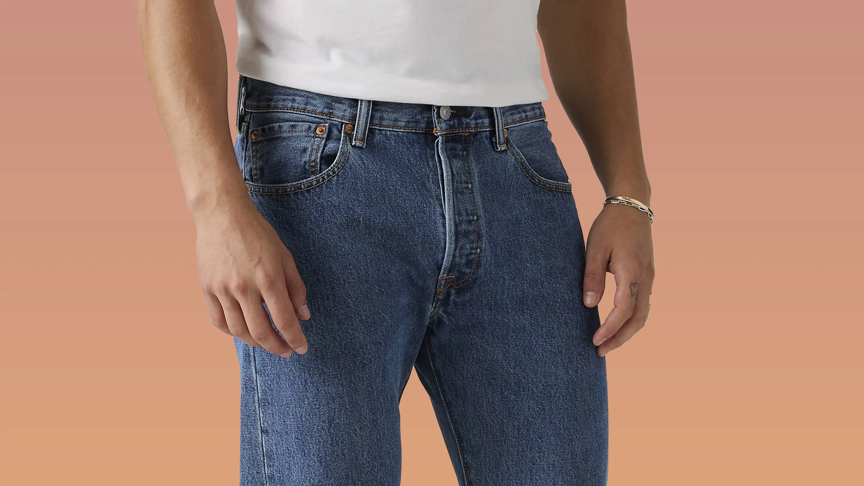 Close-up of blue denim jeans with visible stitching and copper rivets worn with a white shirt.