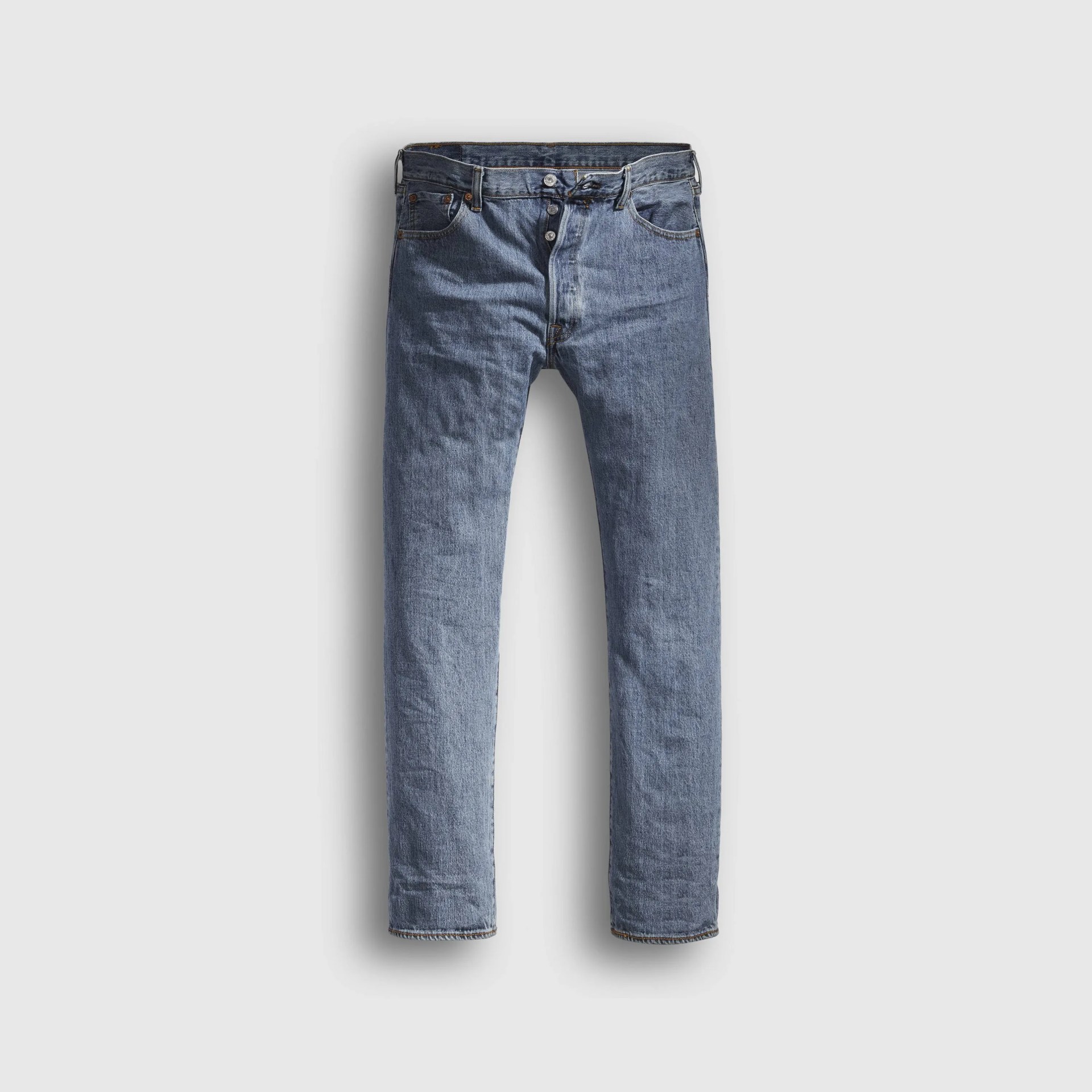 Blue denim jeans with button fly and five-pocket design laid flat on a light gray background.