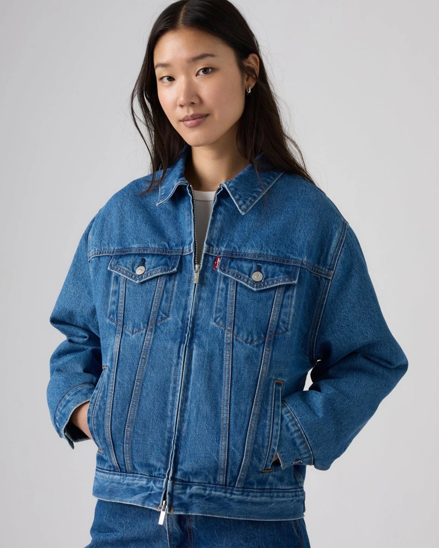 Blue denim jacket with front zipper and flap chest pockets worn by a person.