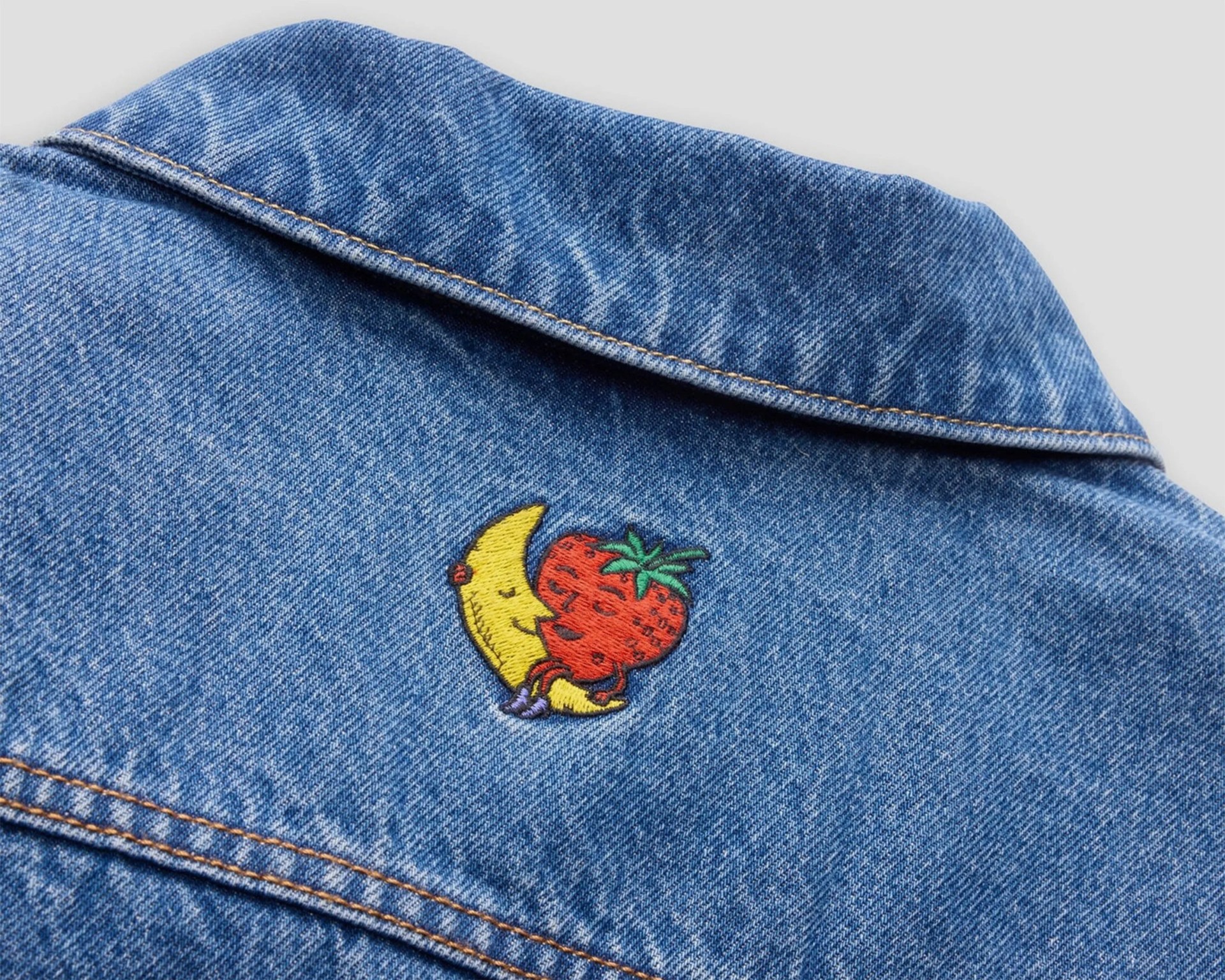 Blue denim jacket collar with embroidered patch of a smiling crescent moon hugging a strawberry.