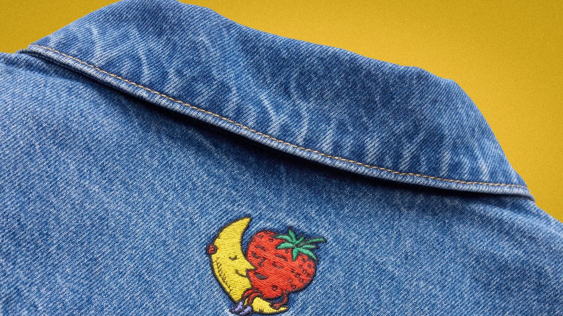 Blue denim jacket collar with embroidered design of a smiling crescent moon hugging a strawberry.