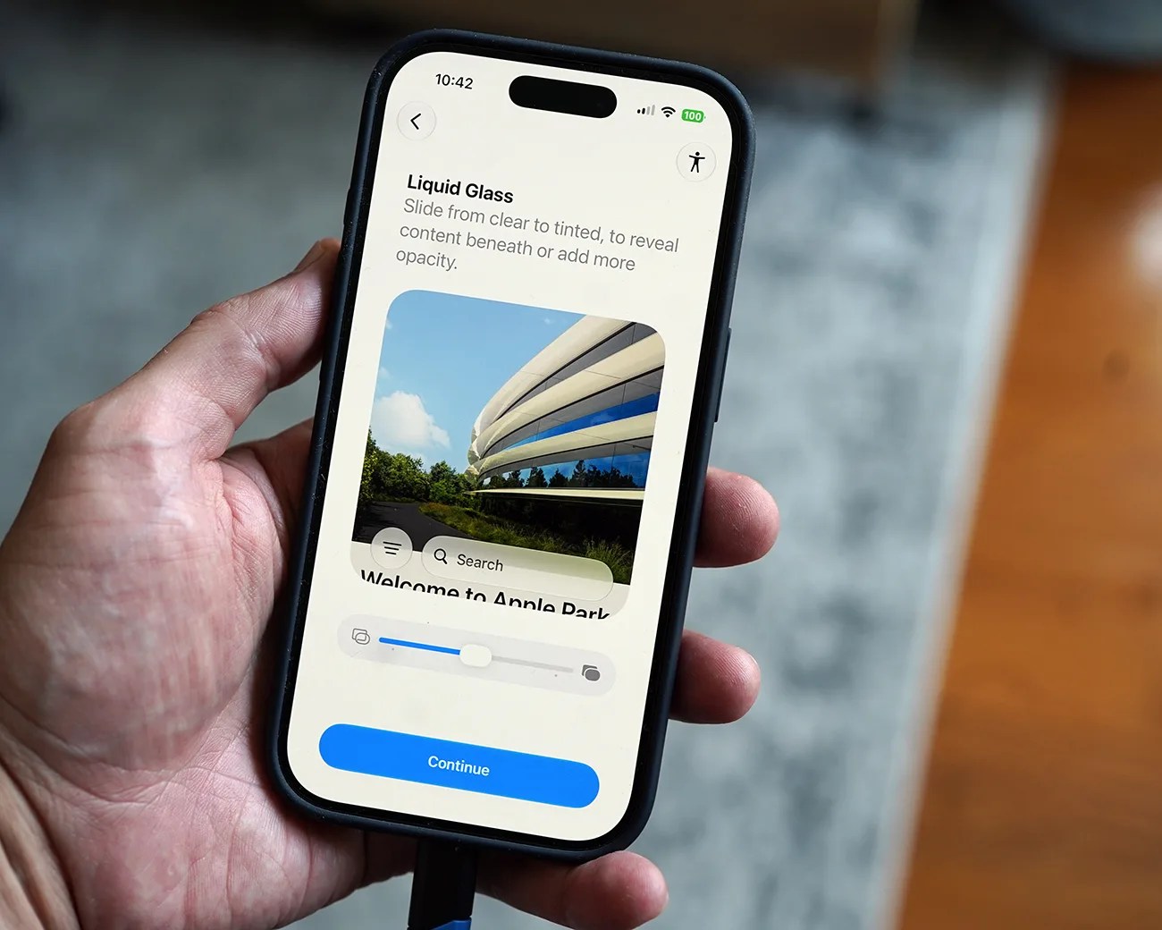 Smartphone held in a hand displaying a screen with "Liquid Glass" text and a photo of a modern building.
