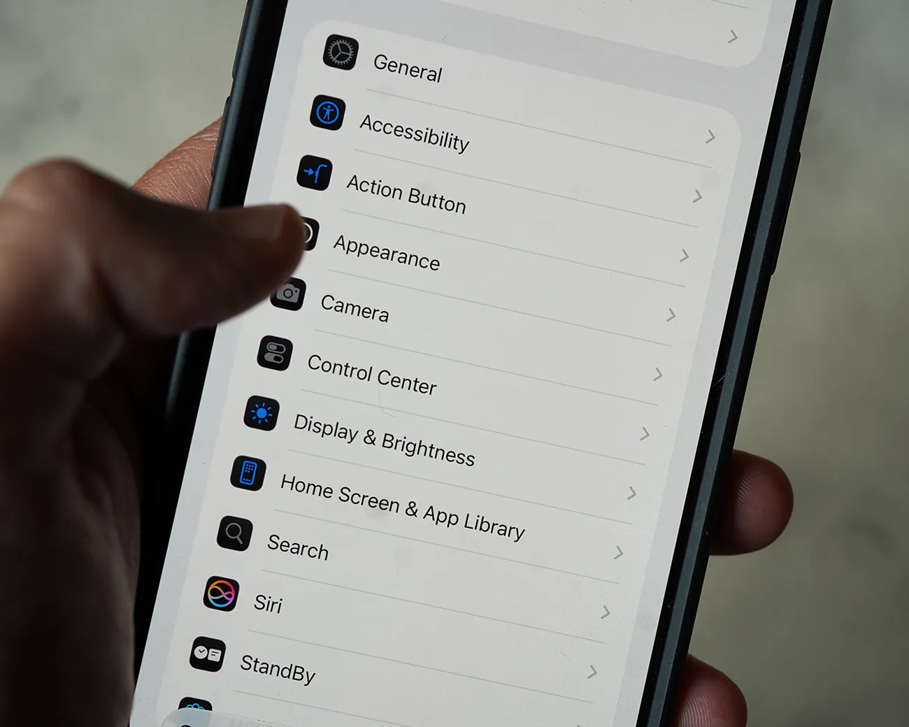 Smartphone screen showing settings menu with options like General, Accessibility, Action Button, and Display & Brightness.