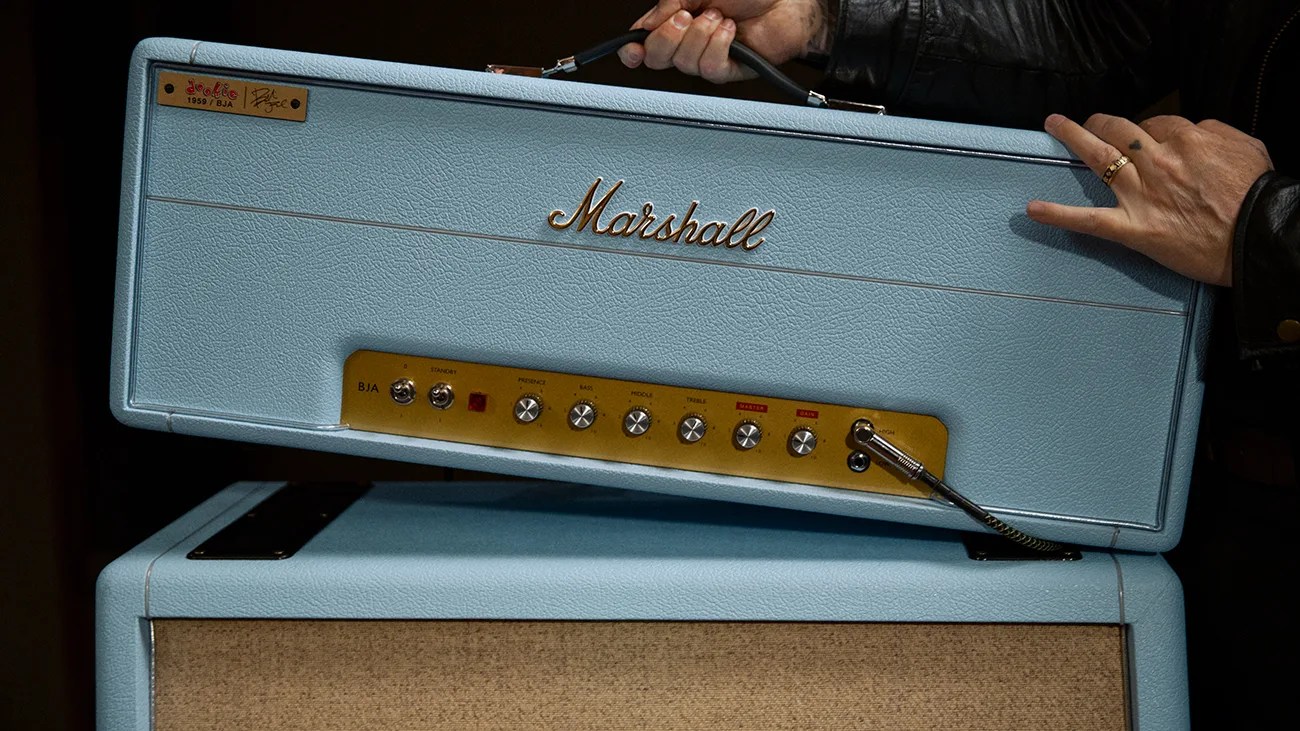 Light blue Marshall guitar amplifier head with gold control panel and knobs, held by a person wearing a black leather jacket.