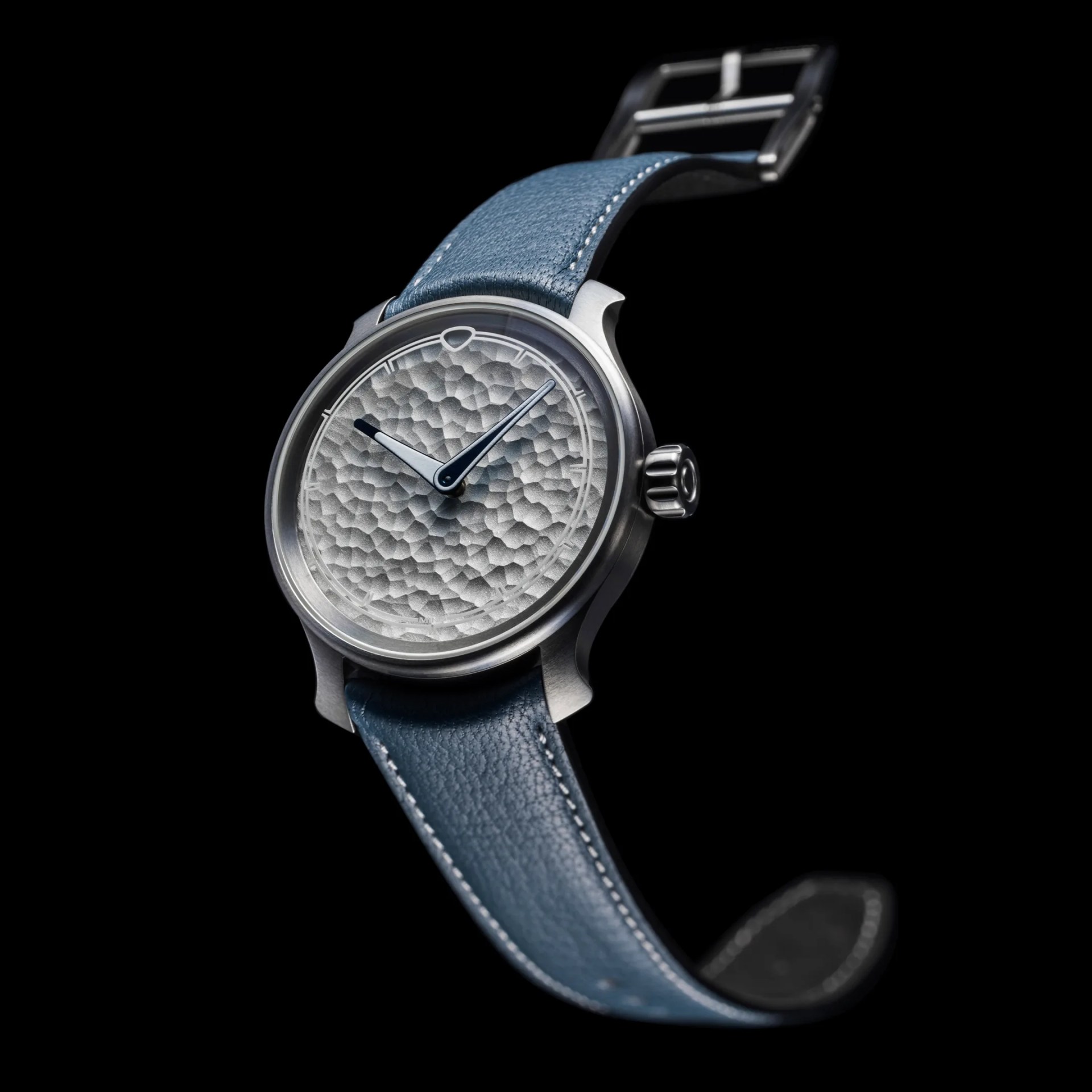 Silver watch with a textured dial and blue leather strap against a black background.