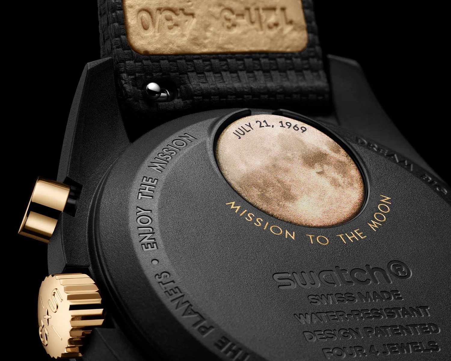 Close-up of the back of a black Swatch watch with gold accents, featuring a moon image and text "MISSION TO THE MOON" and "JULY 21, 1969.