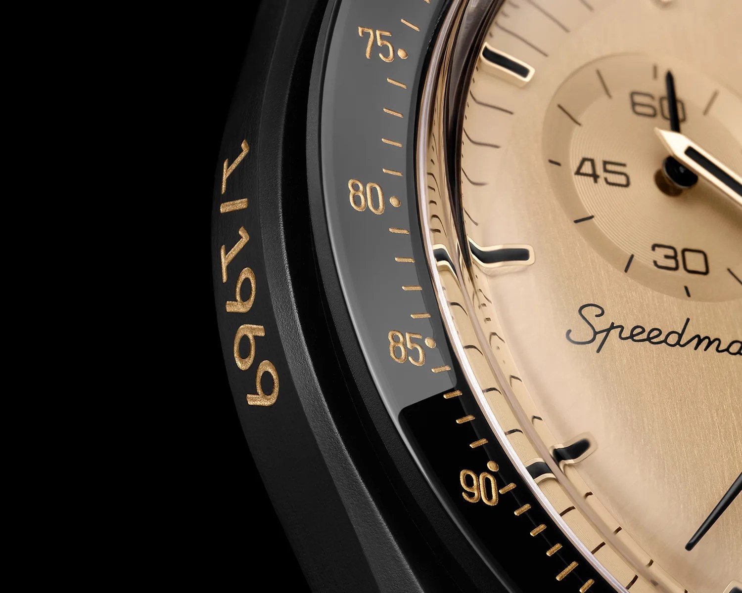 Close-up of a black watch bezel with gold tachymeter markings and a gold dial showing part of the word "Speedmaster".