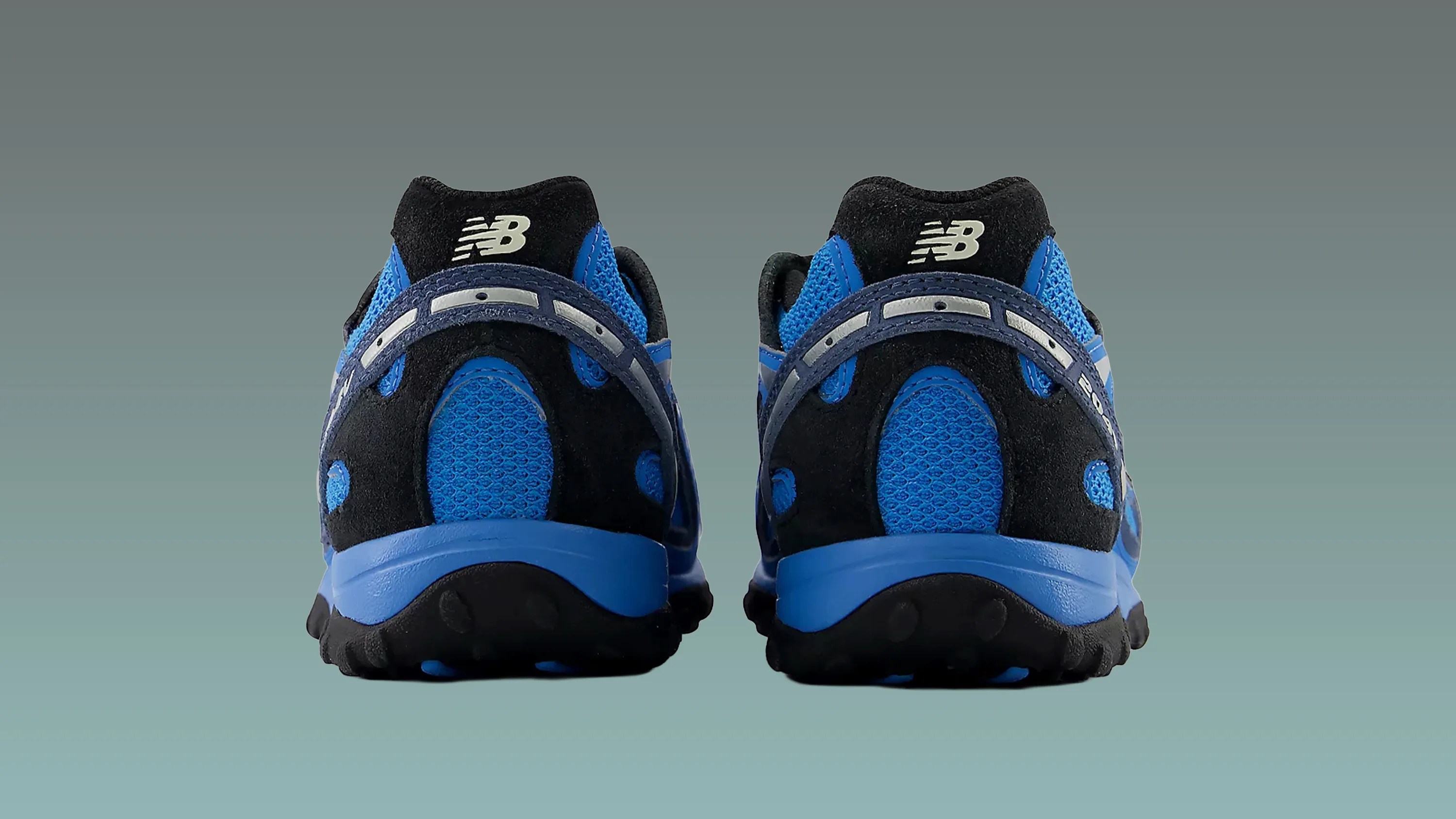 Pair of blue and black New Balance sneakers shown from the back on a gradient gray-green background.