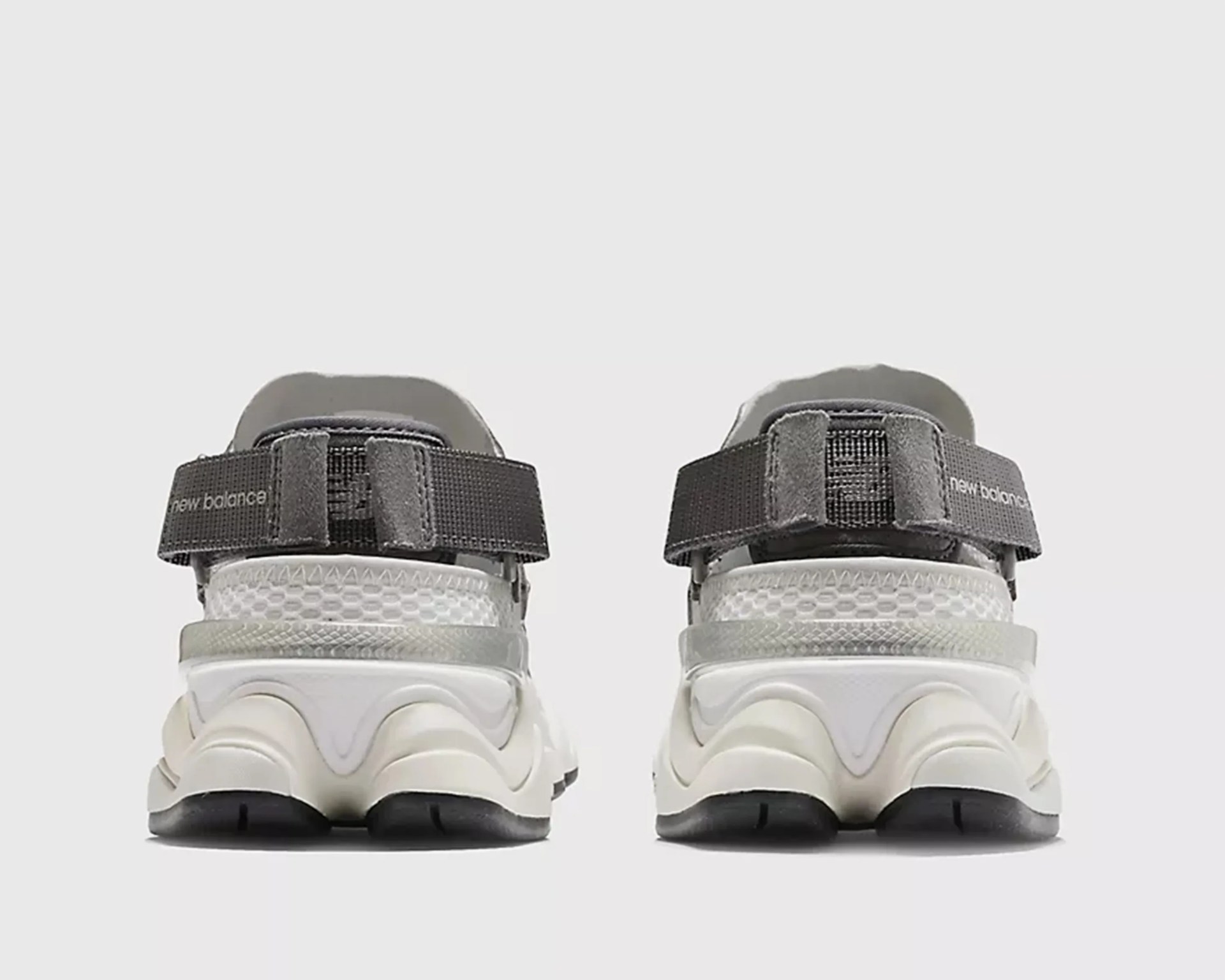 Pair of white New Balance sneakers with black adjustable straps viewed from the back.
