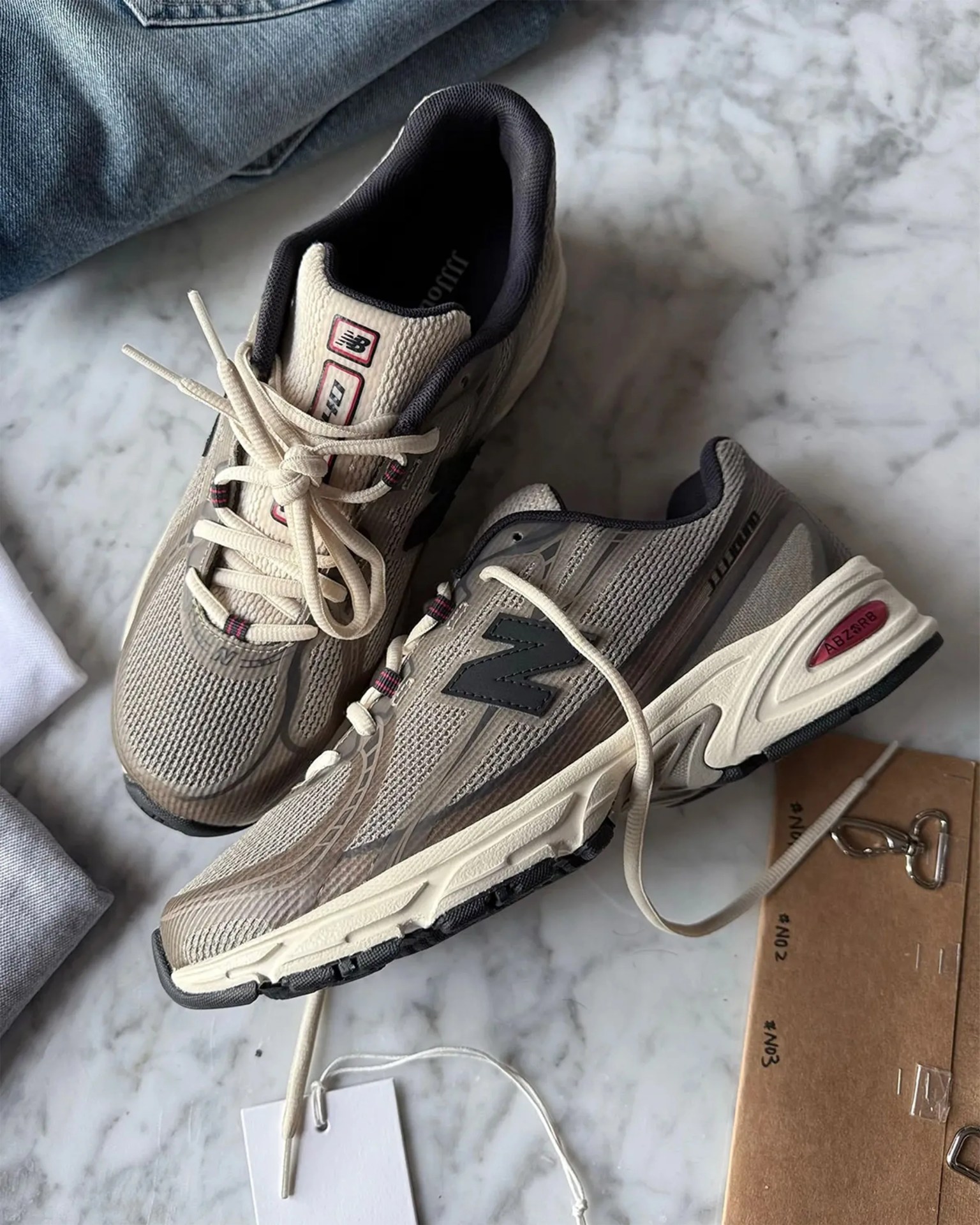 Pair of beige and gray New Balance running shoes with cream laces on a marble surface.