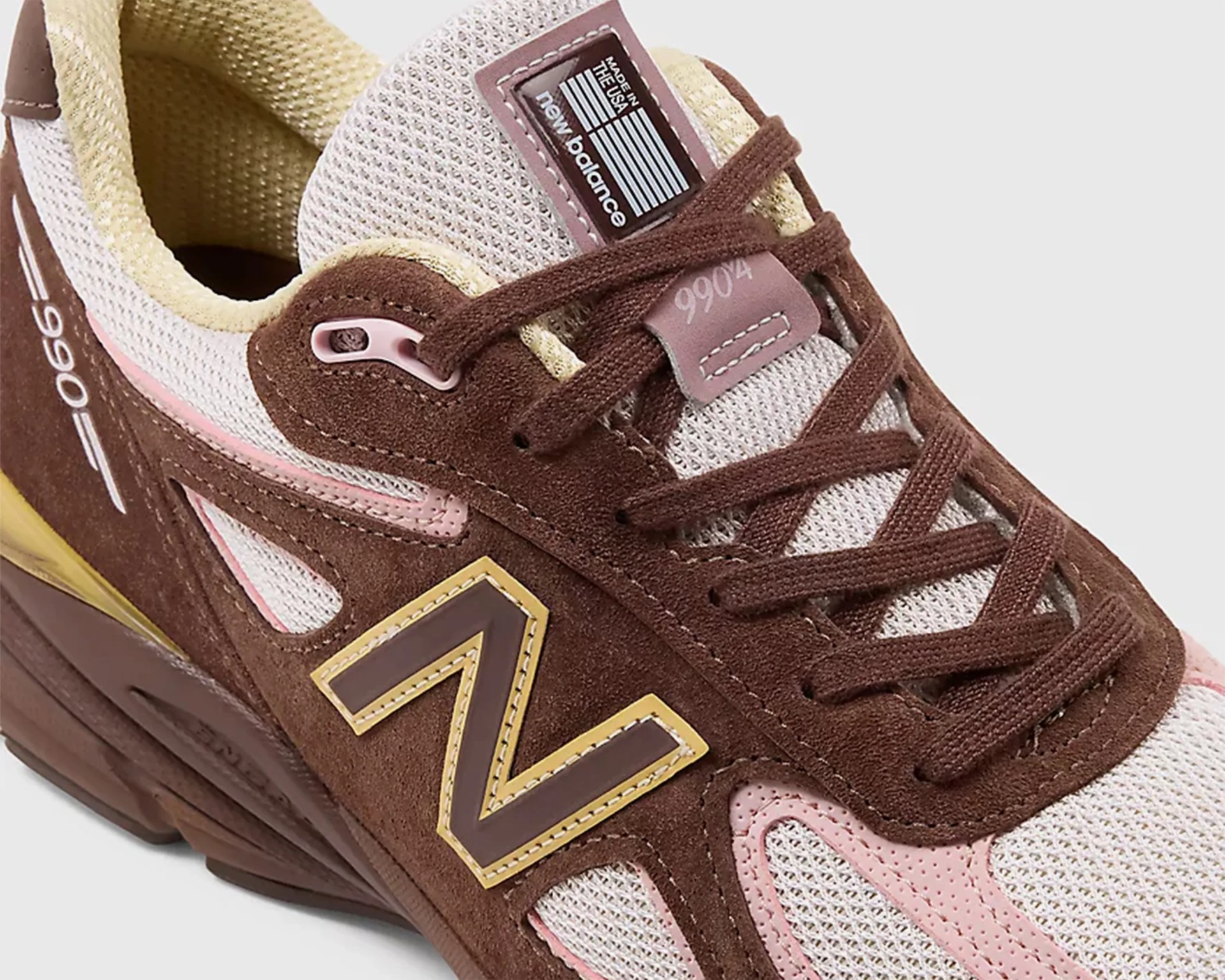 Brown and beige New Balance 990v4 sneaker with pink and yellow accents and brown laces.