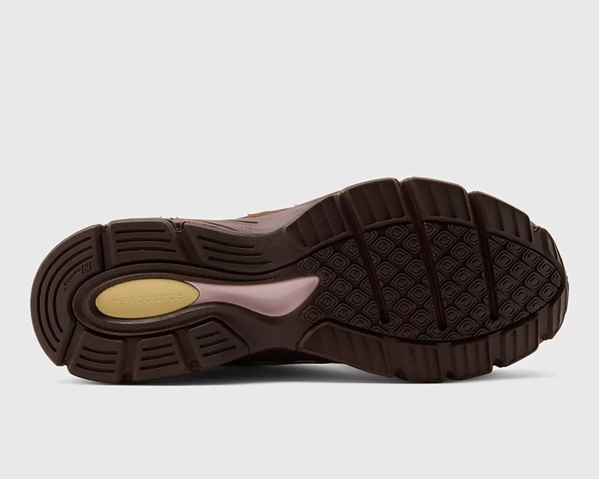 Brown rubber outsole of a New Balance shoe with textured grip and yellow oval logo insert.