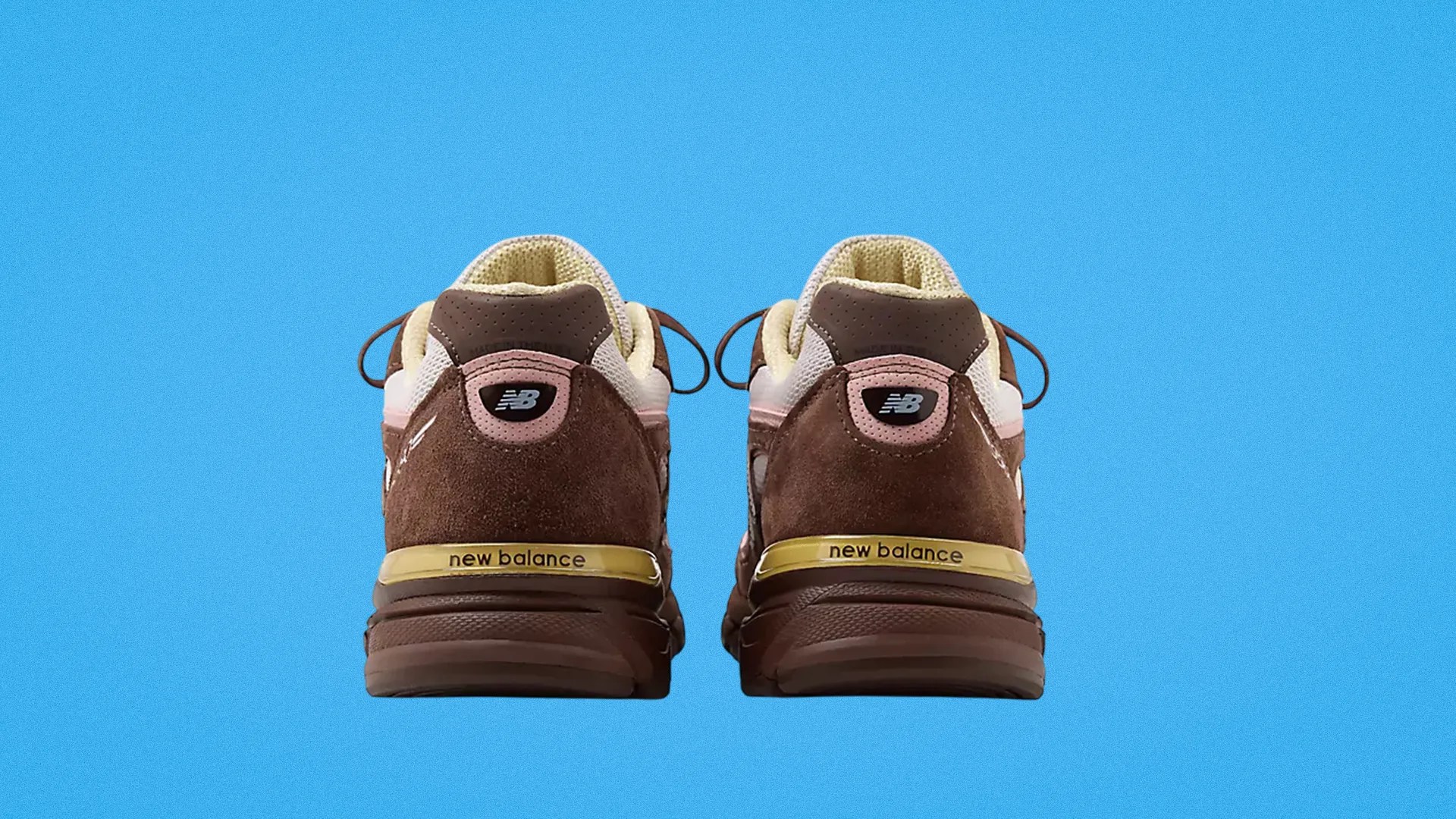 Pair of brown New Balance sneakers shown from the back with beige and pink accents on a blue background.