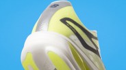 Close-up of the heel of a yellow and gray New Balance running shoe with a white sole against a blue background.