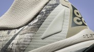 Close-up of a beige and gray textured sneaker with a triangular patch and "42.9" printed on the sole.