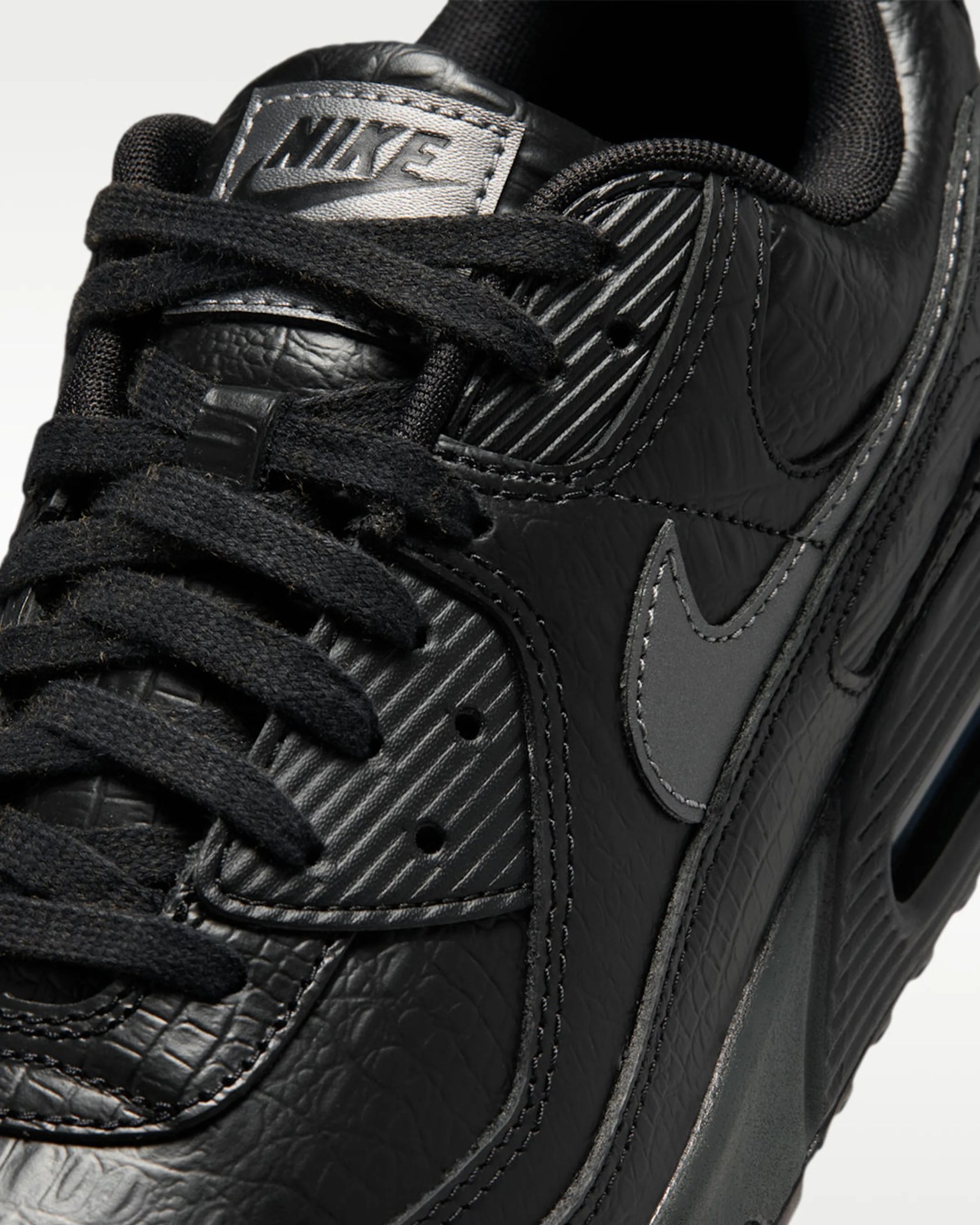Close-up of a black Nike sneaker with textured leather, black laces, and a gray Nike swoosh logo.