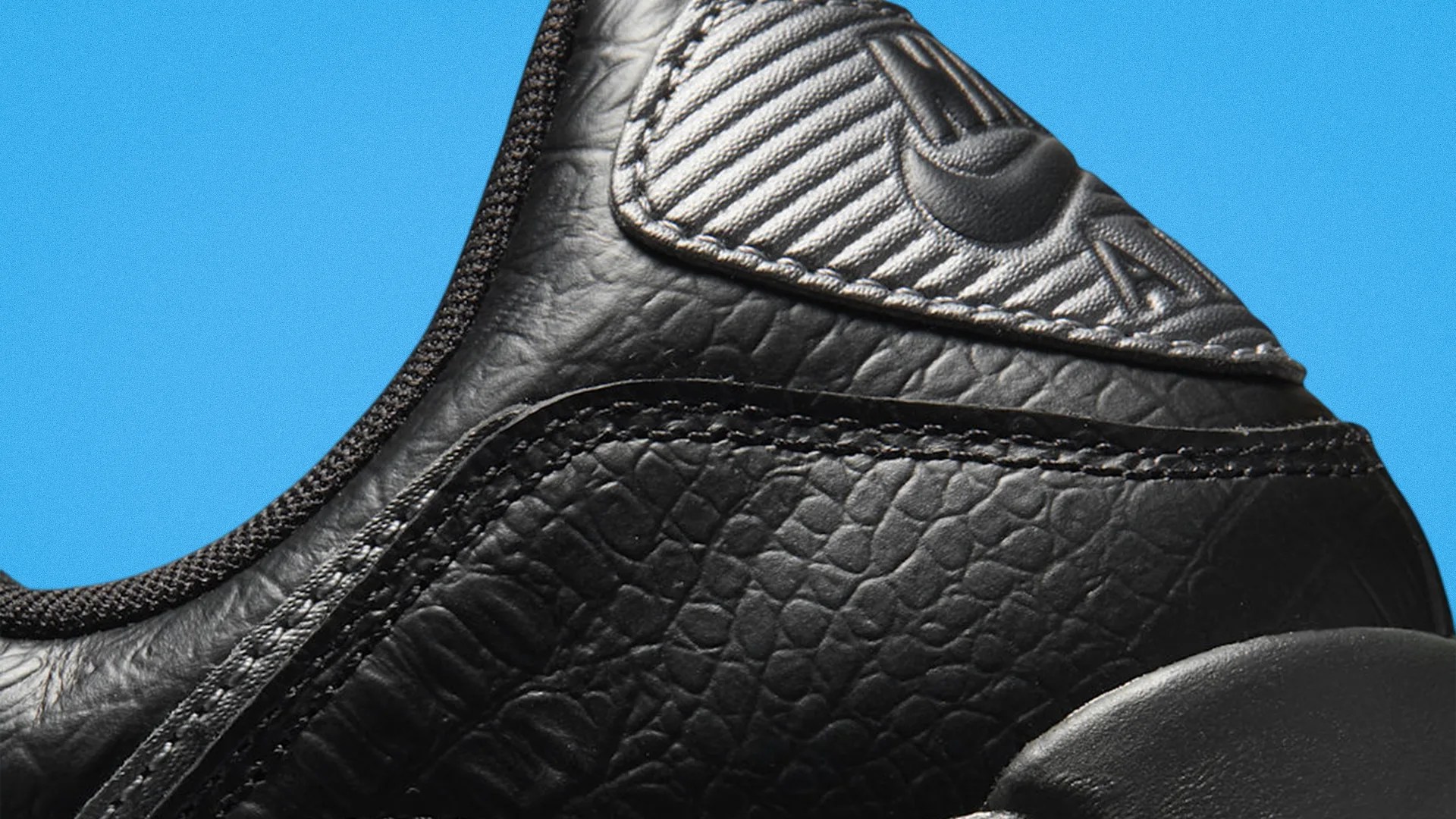Close-up of black textured leather sneaker with stitched detailing and embossed Nike logo on a blue background.