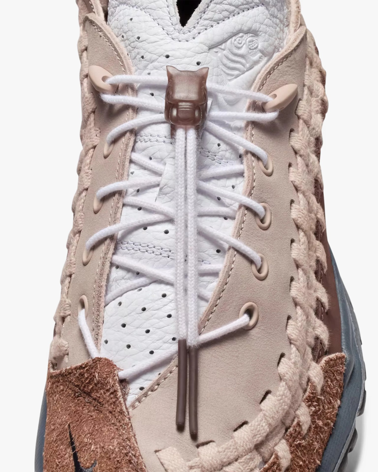 Close-up of a beige and white sneaker with braided detailing, white laces, and a cat-shaped lace lock.