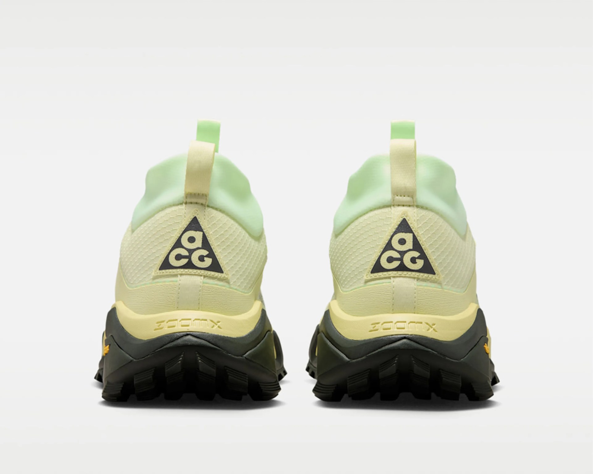 Pair of light yellow and green Nike ACG sneakers viewed from the back with black soles and pull tabs.