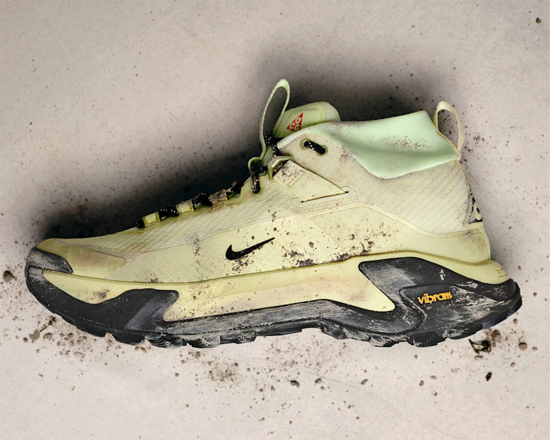Light green and black Nike ACG hiking shoe with Vibram sole and dirt marks on a light surface.