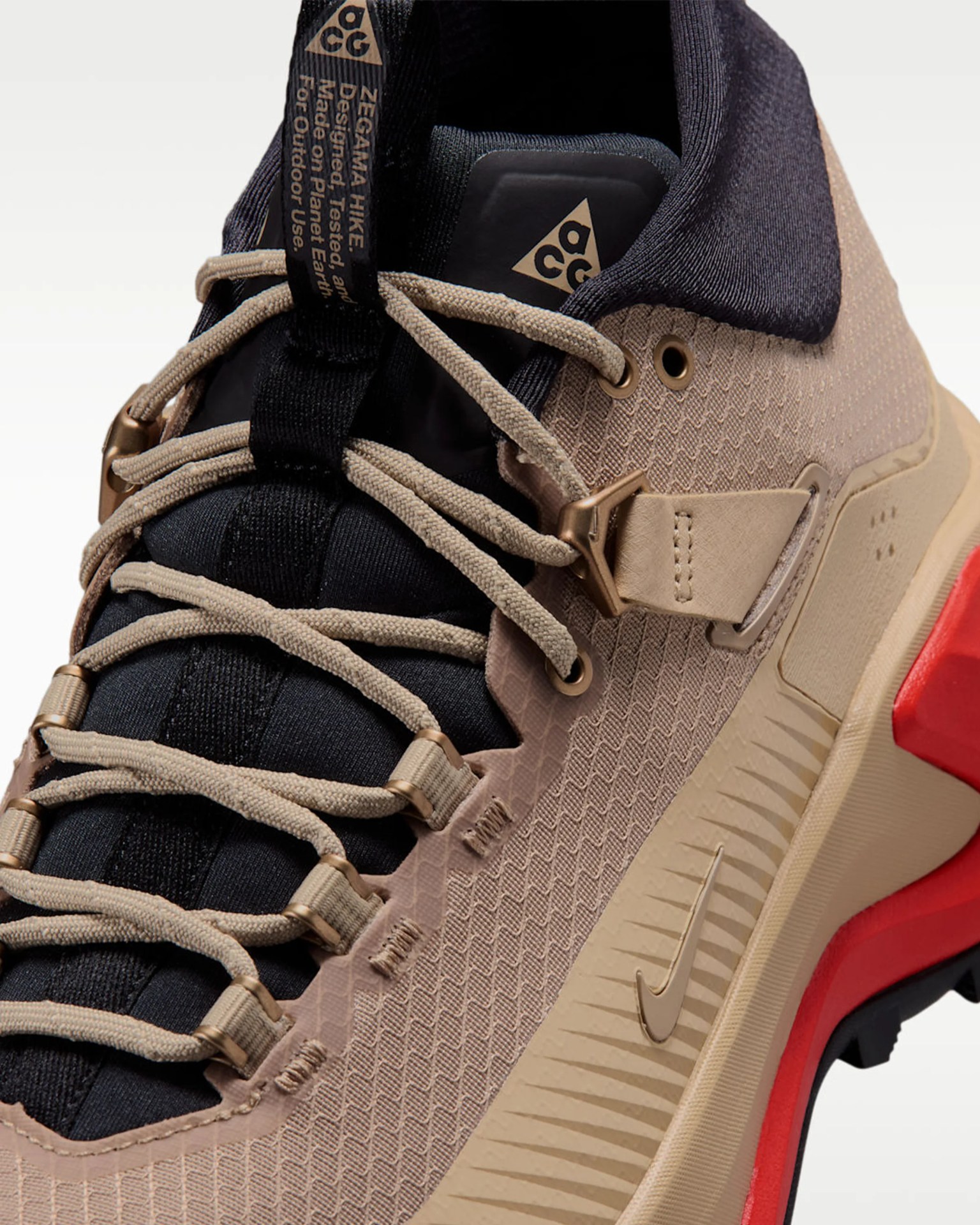 Close-up of a beige and black Nike ACG hiking shoe with beige laces and red accents on the sole.