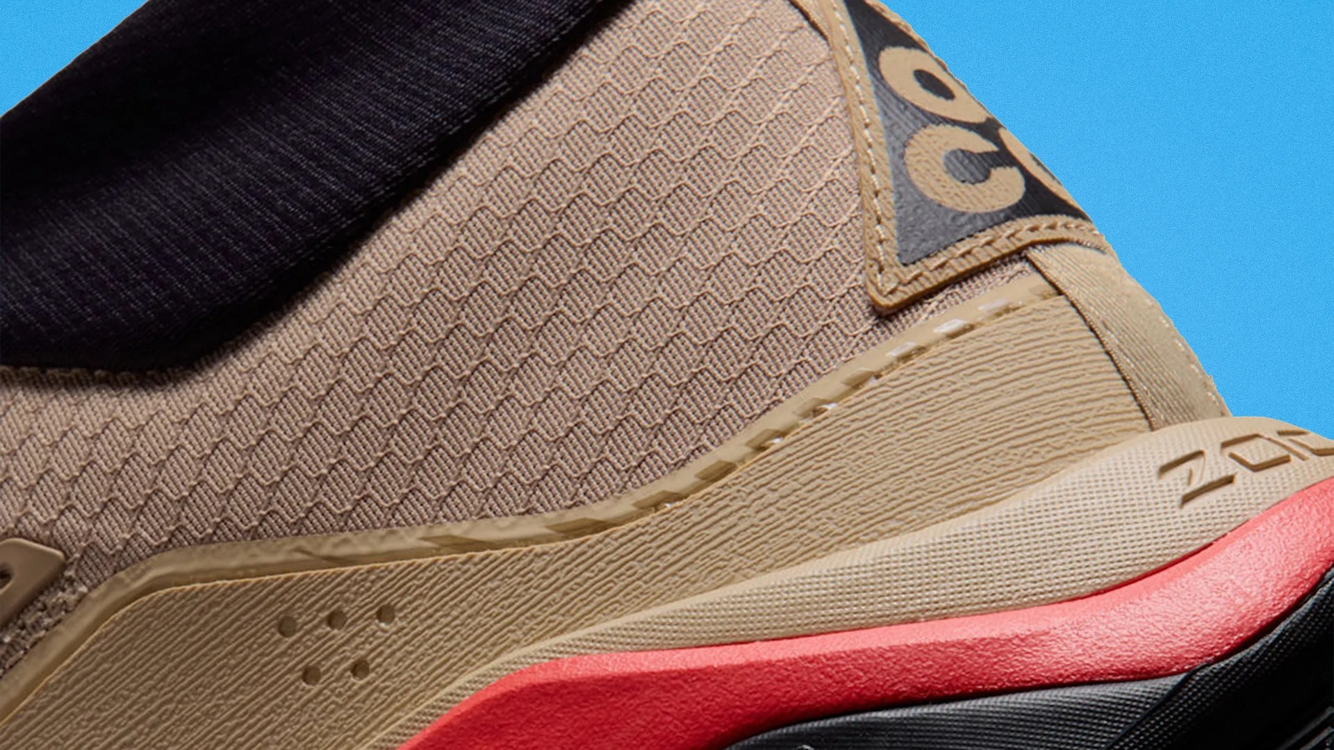 Close-up of a beige sneaker with textured fabric, black collar, and red midsole detail.