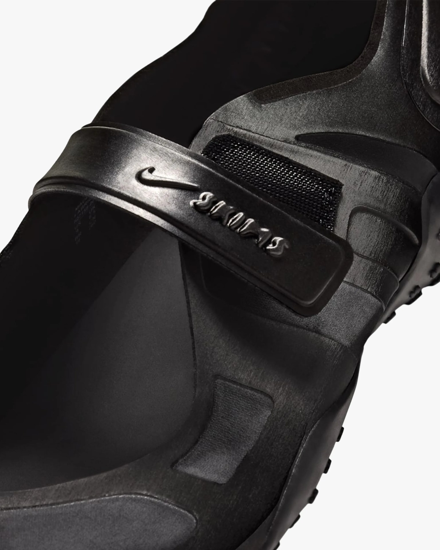 Close-up of a black Nike shoe with a strap featuring the Nike logo and "Swoosh" text.